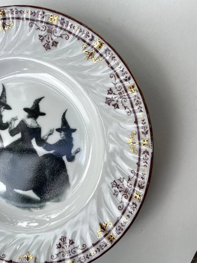 a coven of 3 witches dance hand in hand, the image is victorian in black and white and is printed directly onto an ornate vintage plate