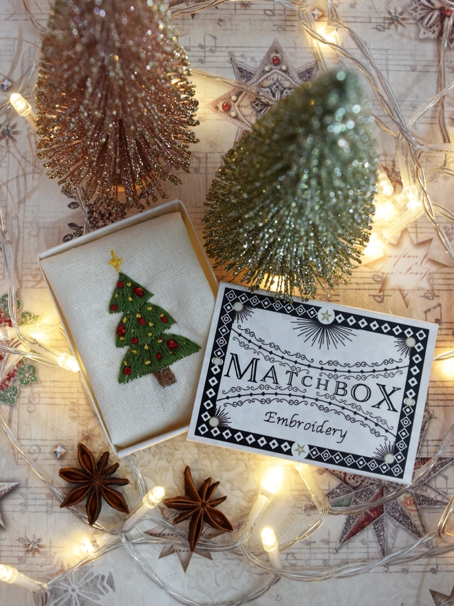 A bright green Christmas tree, displayed in its matchbox with fairy lights miniature frosted trees and star anise.