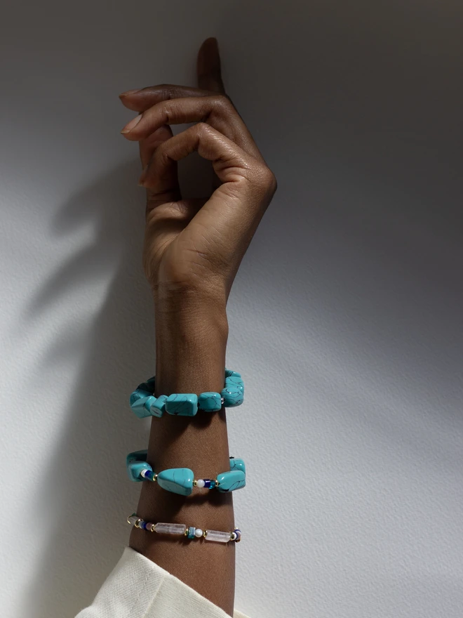 Hand wearing multiple turquoise bracelets on a neutral background