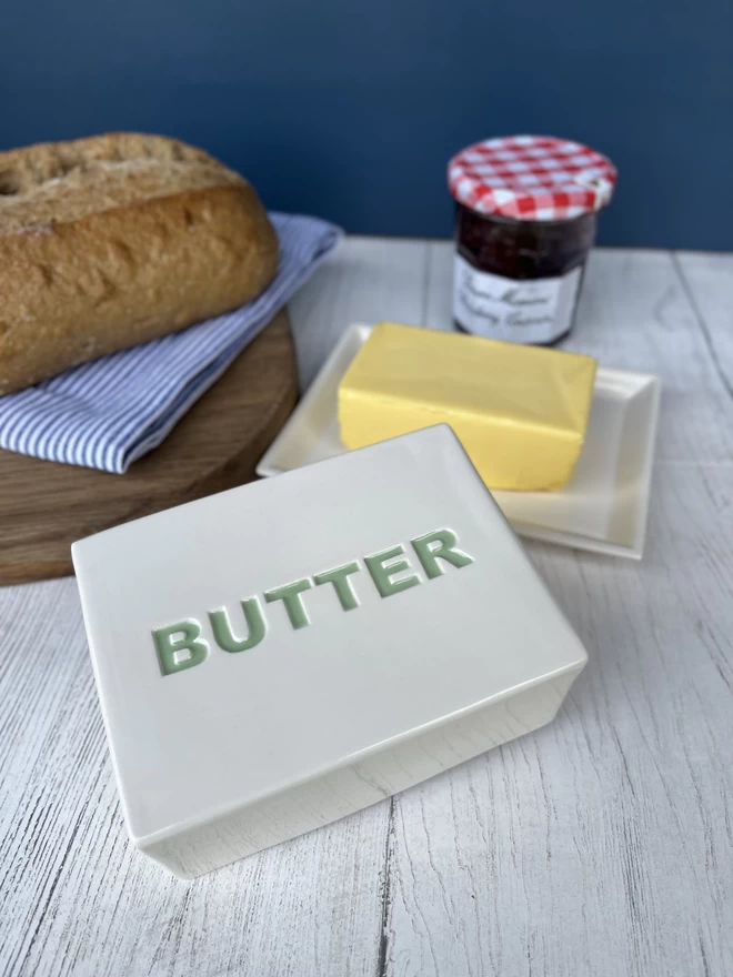 A block of butter sits on a handmade ceramics dish. The top of the lid has ‘butter’ painted in green.