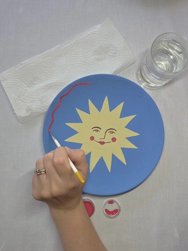 a hand painting a sun design onto the blue paint. 