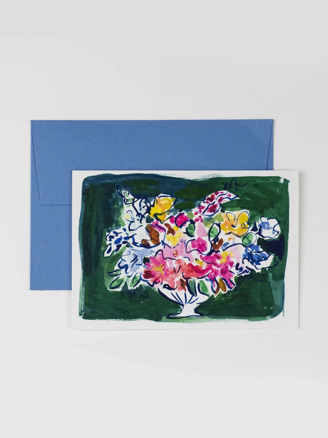 An illustrated greetings card featuring an  expressive ink painting of a colourful bouquet on a dark green envelope. The card is photographed with it's corresponding light blue pale envelope