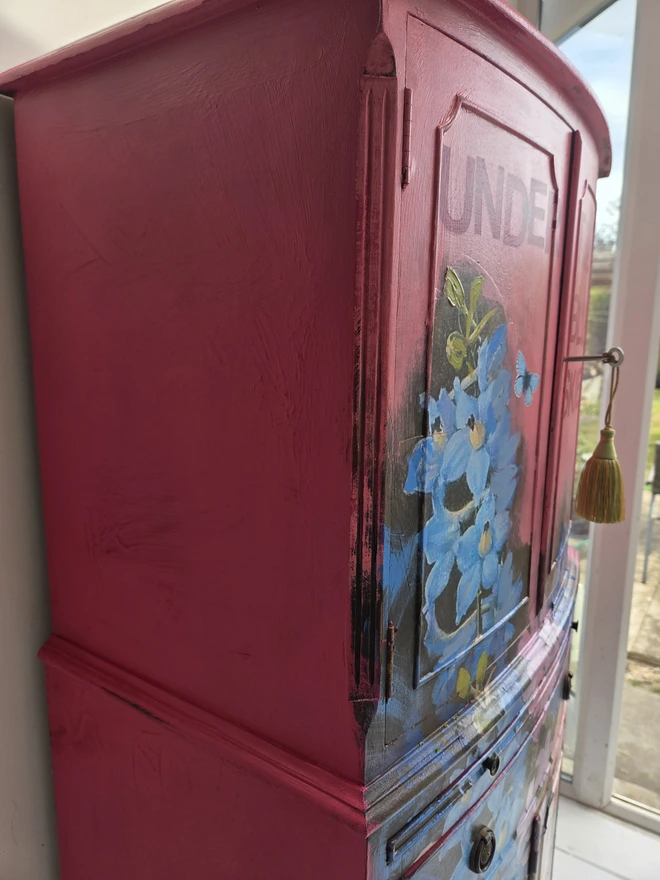 Side view of painted vintage wooden cabinet with pink, blue and floral decoration
