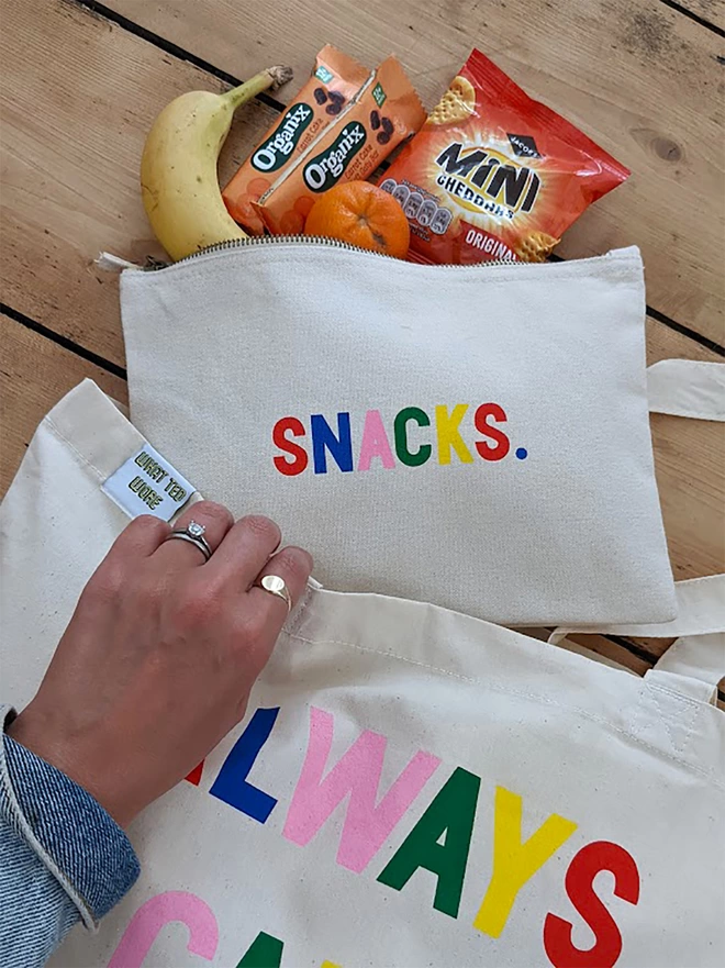 A canvas pouch on a wooden floor with multi coloured 'Snacks' slogan