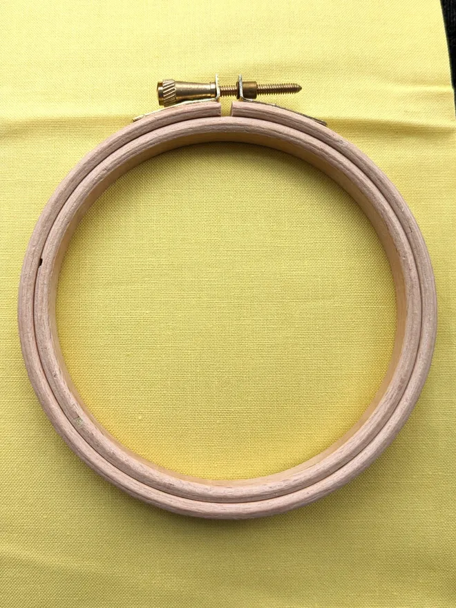 A wooden embroidery hoop lying on a piece of yellow coloured fabric