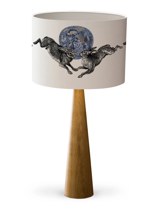 Drum Lampshade featuring a pair of hares leaping across a blue and silver moon with a white inner on a wooden base on a white background