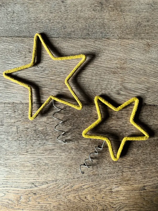 A small and a large gold string covered wire star with a coil for topping a Christmas tree on an oak table