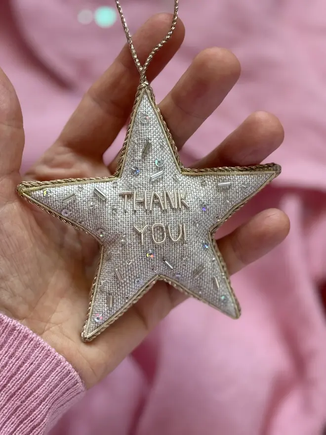 embroidered linen 'thank you' star decoration. silver beaded embroidered star decoration photographed against pink background.
