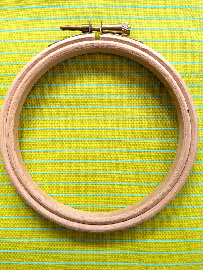 A wooden embroidery hoop lying on a stripy yellow fabric