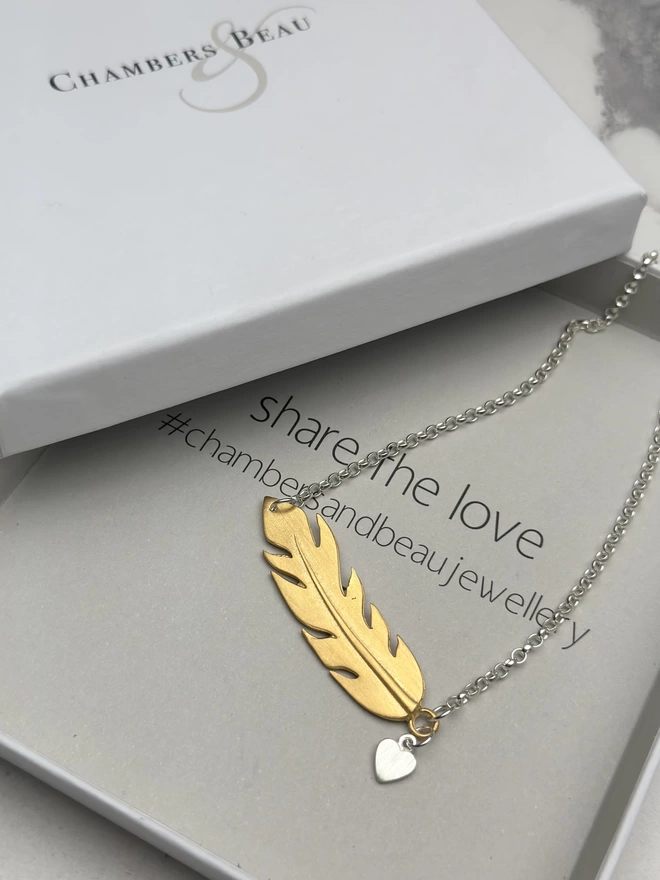 sterling silver chain with gold horizontal feather charm. a small silver heart charm hangs from the chain next to the feather