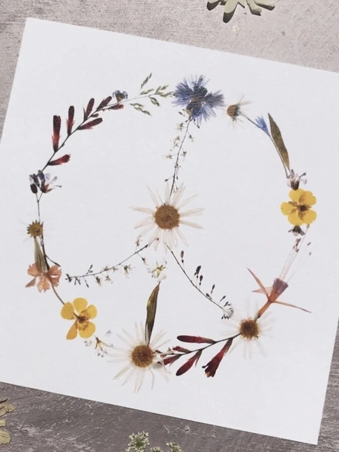 Pressed Wildflower Peace Sign Print, a wildflower peace sign print sitting against a stone surface. 