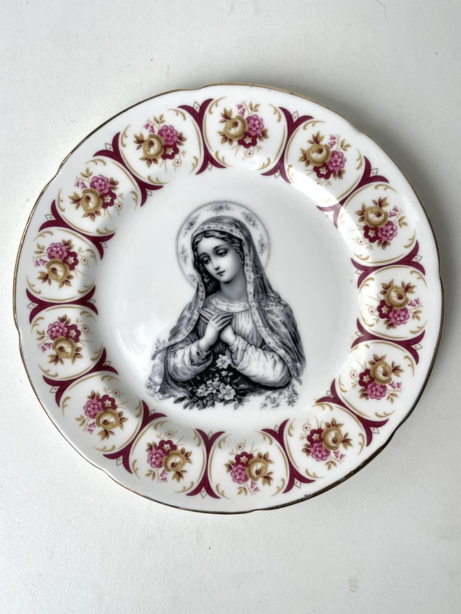 a vintage plate with a really ornate border has the victorian black and white illustration of the virgin mary in the centre