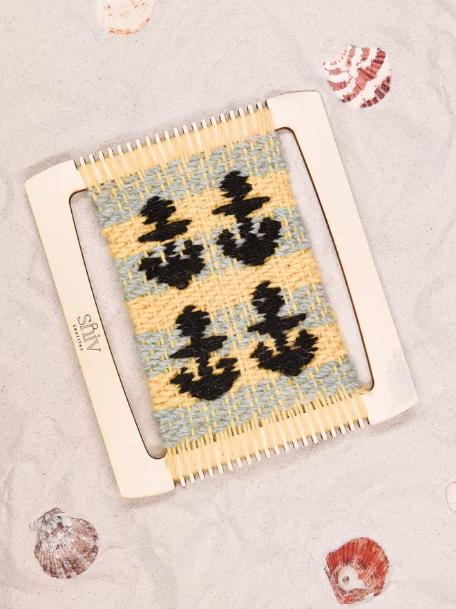 seaside weaving kit. a yellow and grey weave piece with black anchors photographed on a loom.