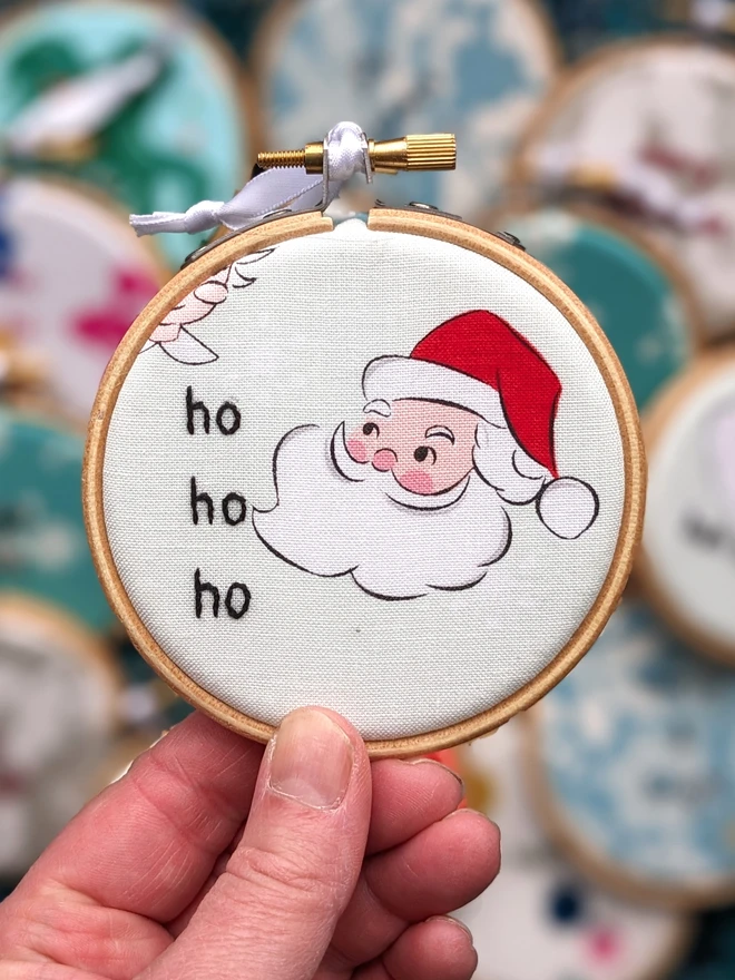 A hand embroidered hoop on Christmas fabric reading ho ho ho