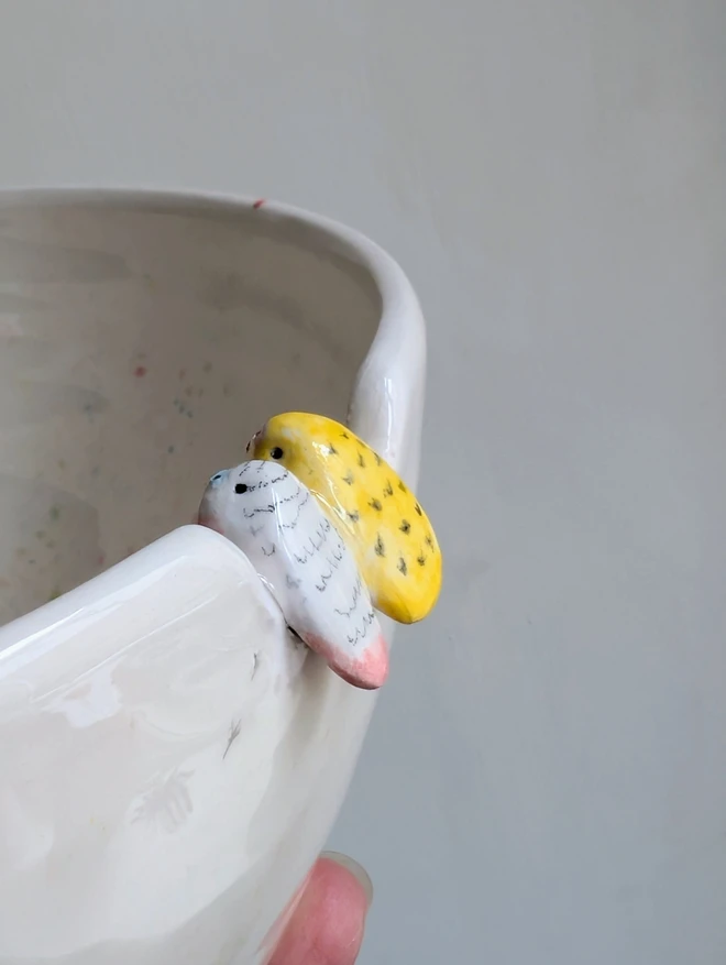 ceramic budgies perching on the edge of a large pottery bowl in yellow and pink