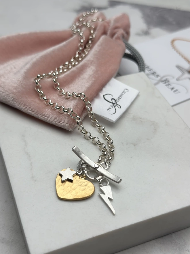 Large hammered gold heart and small silver star and electric bolt hanging from sterling silver chain with silver T-bar fastener