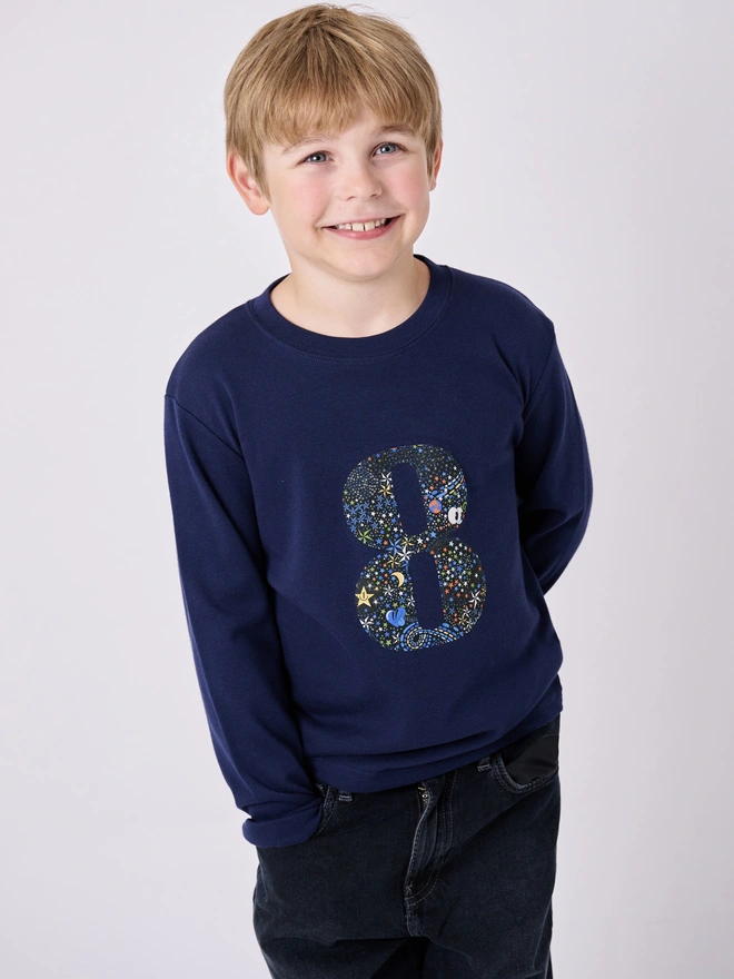 an 8 year old boy wearing a navy cotton t-shirt with a number 8 in a star print fabric sewn on the front