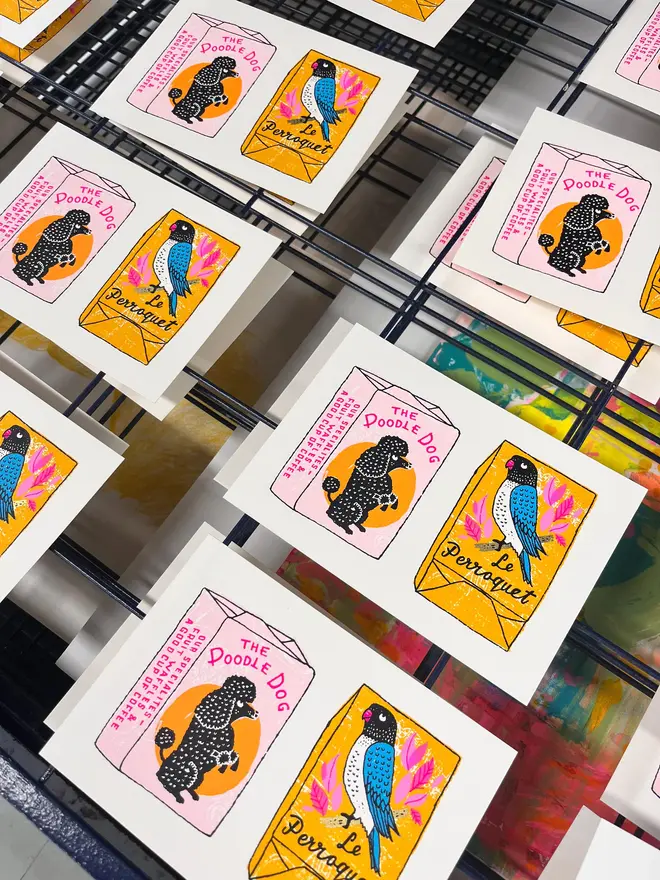 Parrot And Poodle Sugar Cube Screenprint Sugar Sugar, a pair of colourful sugar cube designs, they sit on a studio rack. 