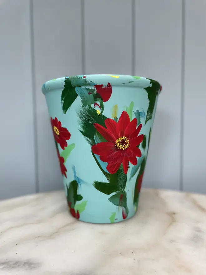 Unique hand-painted terracotta pot featuring vibrant red zinnias on a light blue background