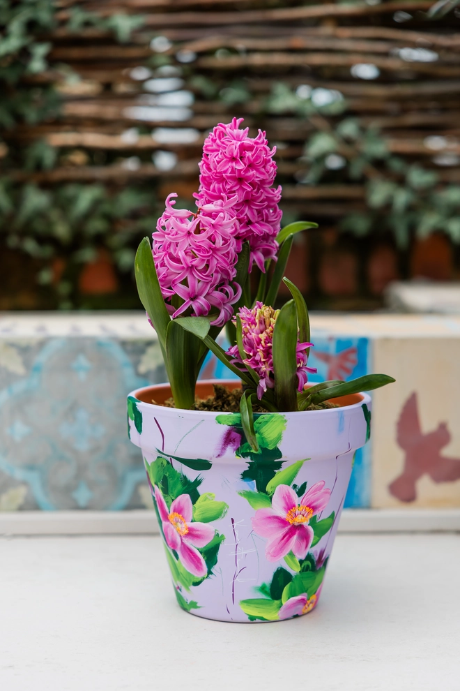 A beautifully hand painted interior terracotta plant pot. Background painted in a pale lilac adorned in pink Japanese anemone. 