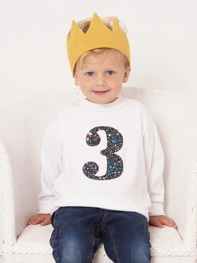 3 year old boy sitting wearing a white long sleeve t-shirt with a number 3 sewn on in Liberty Fizz Pop Black print 