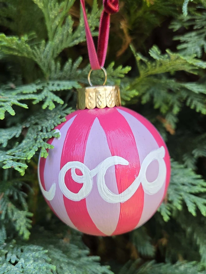 hand painted pink stripe bauble with name personalisation, hanging on a christmas tree