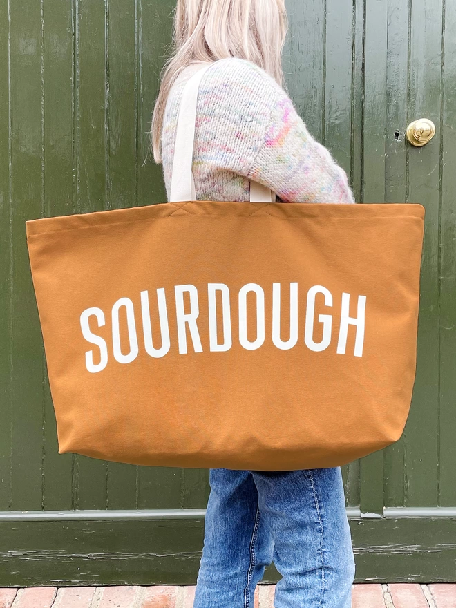 model carrying an oversized tan canvas tote bag with sourdough slogan