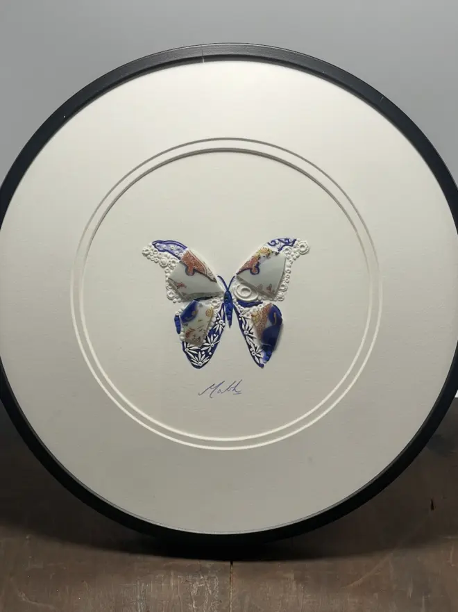Hand-drawn, painted, mosaic clay, vintage Japanese pottery insect on white double mounted card, in a black circular frame.