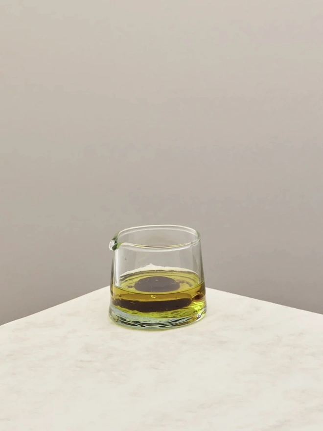 Low Jug, a small glass jug sitting on a counter top against a plain backdrop. It is filled by balsamic vinegar. 