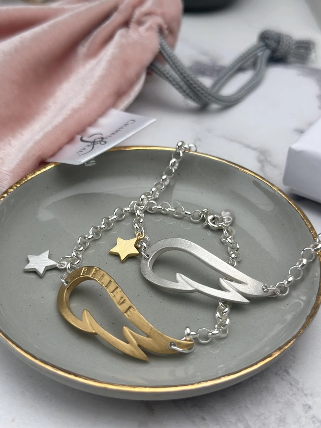 sterling silver charm bracelet with large silver wing charm and small gold star on silver chain and a personalised gold wing charm bracelet on sterling silver chain with silver mini star charm