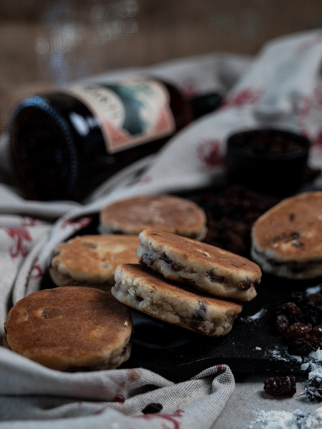 Loose Barti Rum and Raisin Welsh Cakeson black griddle with a welsh dragon and beige table cloth and bottle of Barti Rum in the background
