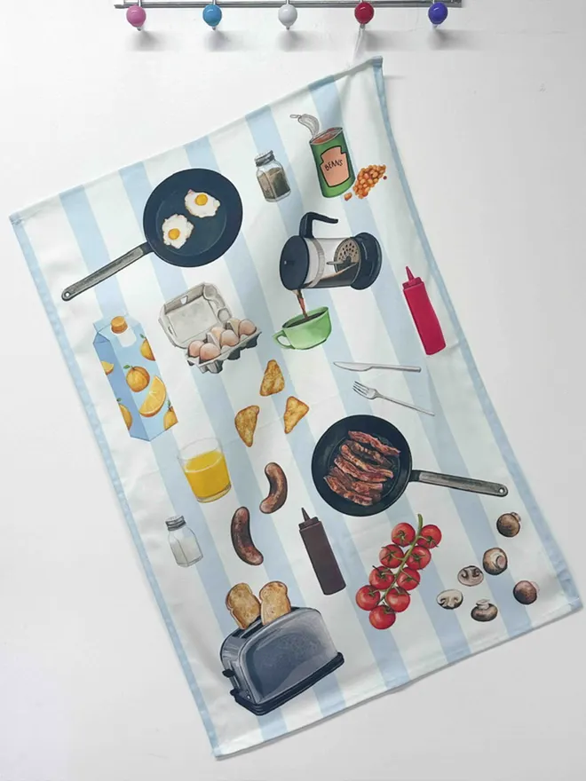 Hanging blue striped tea towel with breakfast brunch themed items - coffee, egg, orange juice, sausages, tomatoes