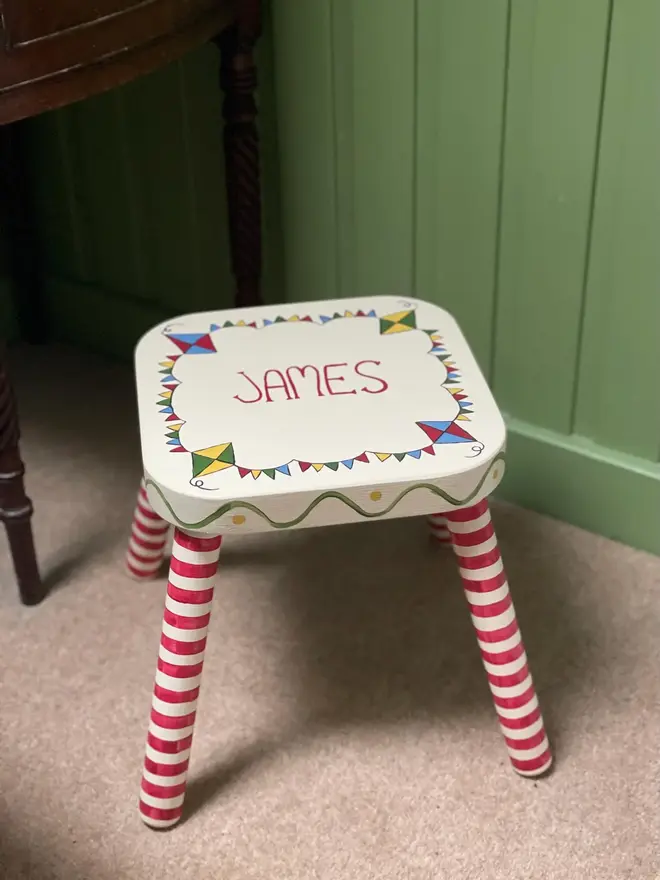 personalised hand-painted nursery stool. a small white stool with red and white striped legs, painted with 'james' on top.