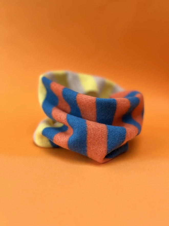 Blue Orange Yellow knitted snood shown from side angle on an orange background