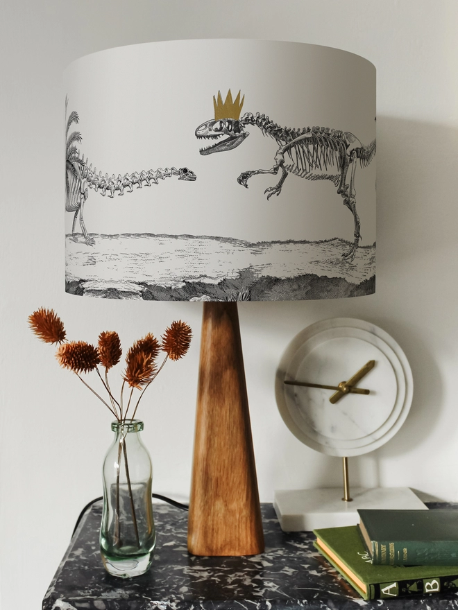 Drum Lampshade featuring Dinosaurs on a wooden base on a shelf with books and ornaments