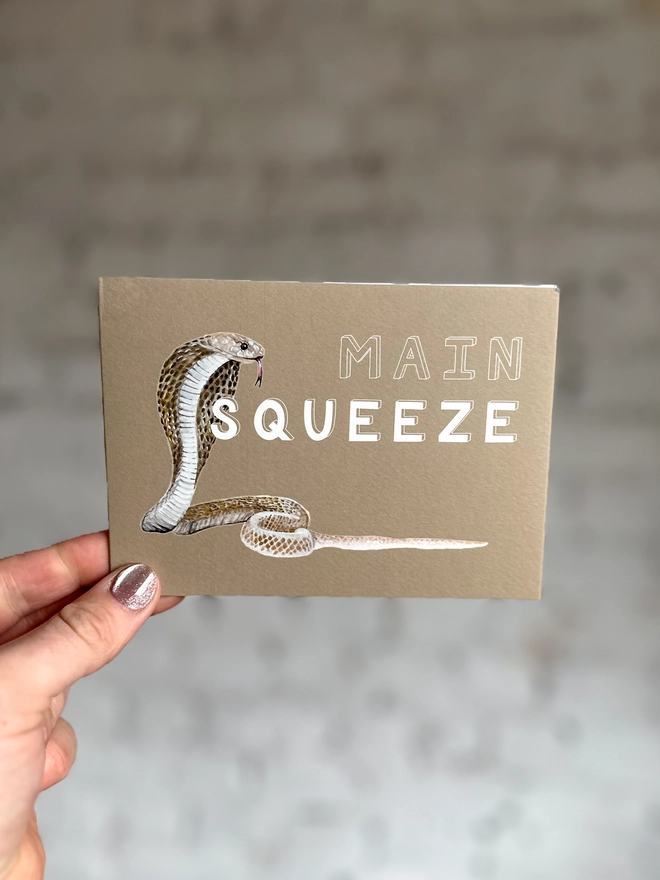 a beige greetings card featuring an illustration of a cobra with the text “main squeeze”