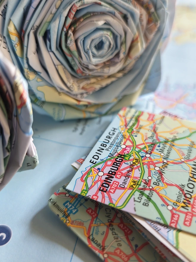 Real Paper Map Roses - Custom Destination. a bouquet of paper roses made from old maps, photographed on top of other maps.