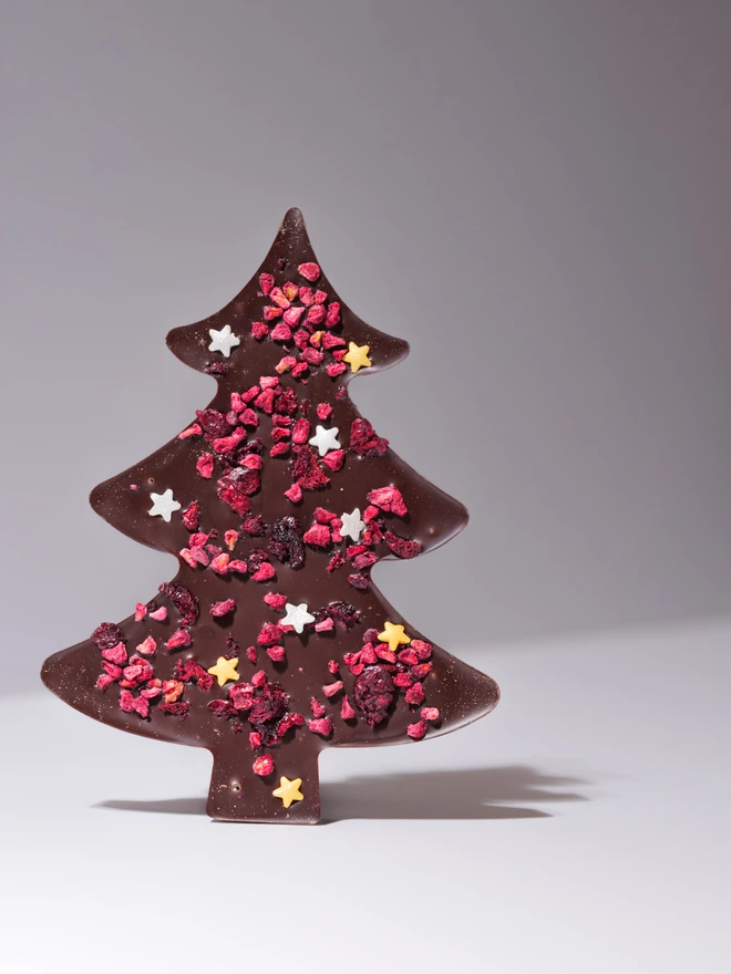 a solid dark chocolate christmas tree shape, sprinkled with raspberry pieces and edible stars