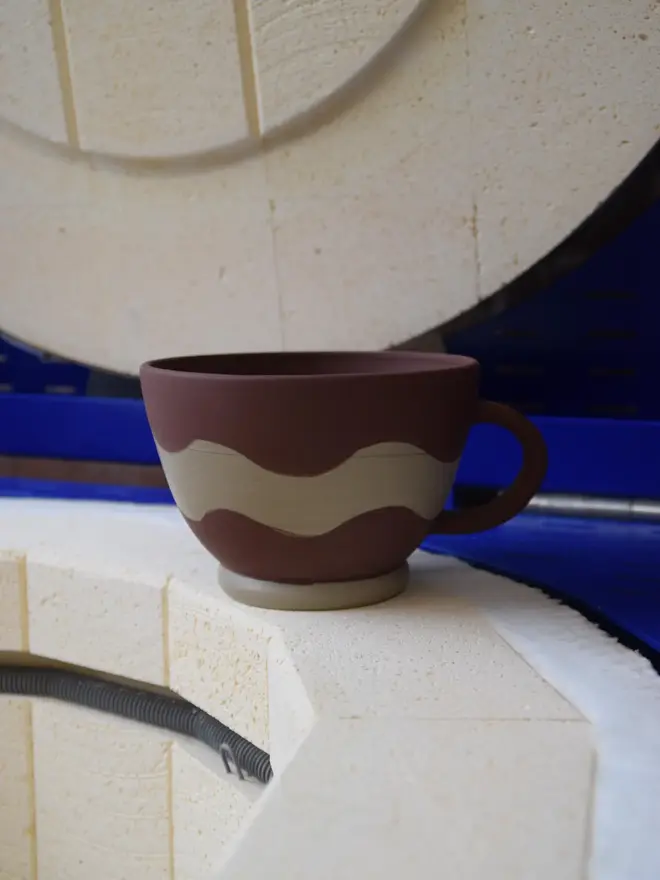 Handmade ceramic Ripple Mug — brown and cream design pictured inside kiln
