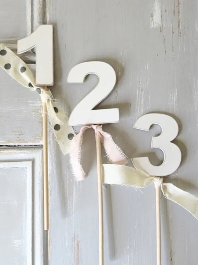 hand painted wooden number cake topper. three white number cake toppers with ribbons.