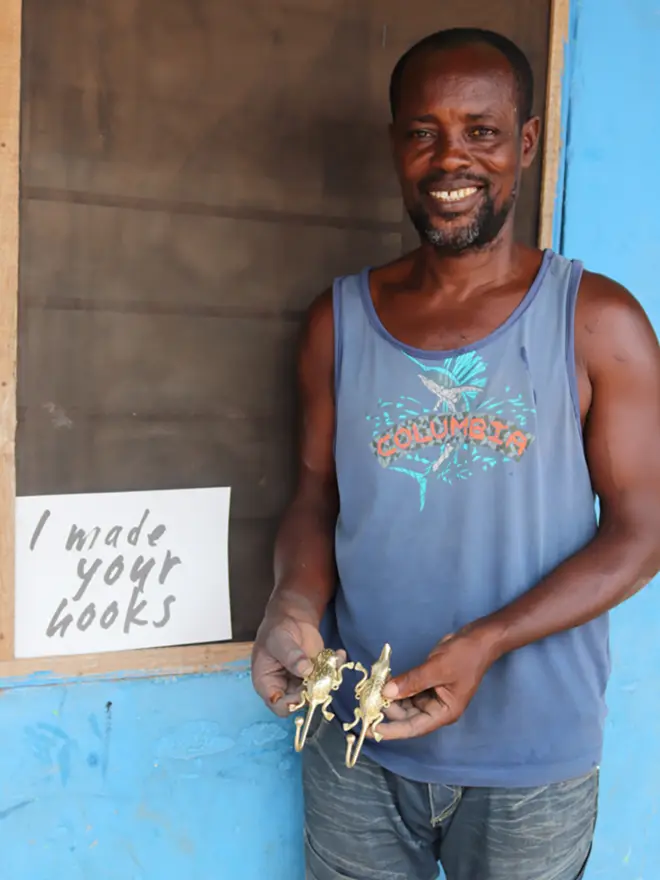 George stands smiling with a sign that reads "I made your hooks"