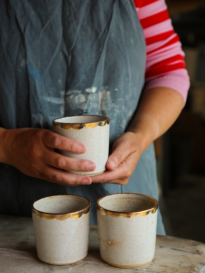white stoneware drinking beaker with gold scallop decoration around the rim