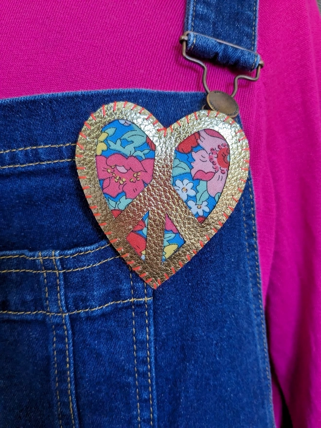 Gold and floral peace sign heart brooch worn on denim dungarees