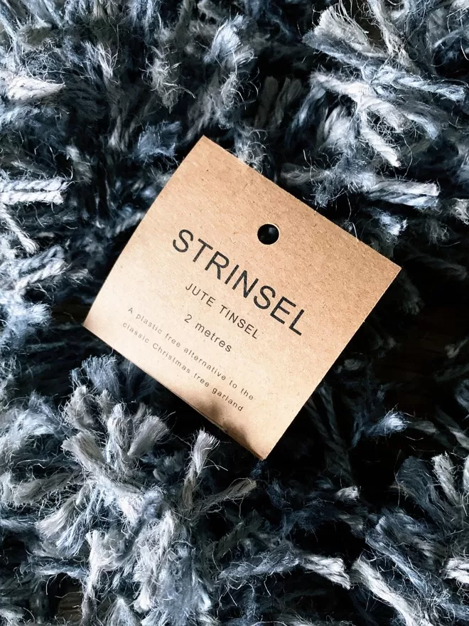 A tumble of silver dyed jute string tinsel AKA Strinsel packaged in a kraft card label on an oak table