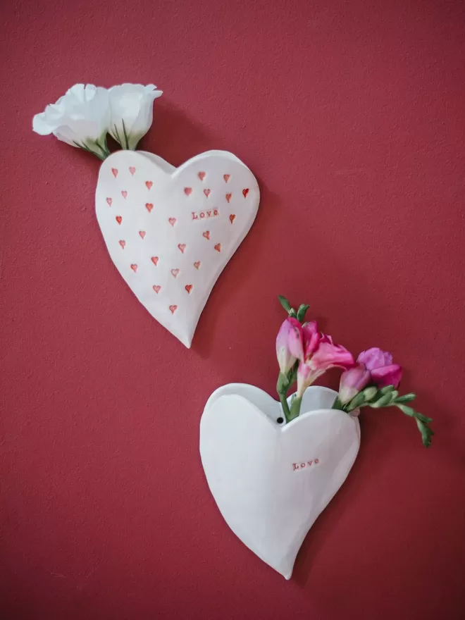 Ceramic heart seen hung on the wall with flowers in them.