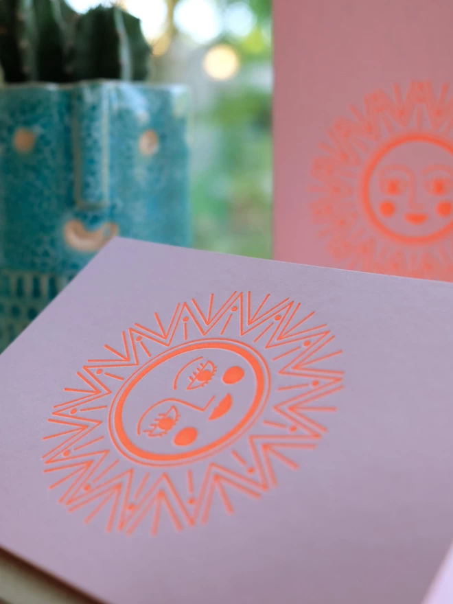Close up of neon orange ink sunshine illustration on pink card.