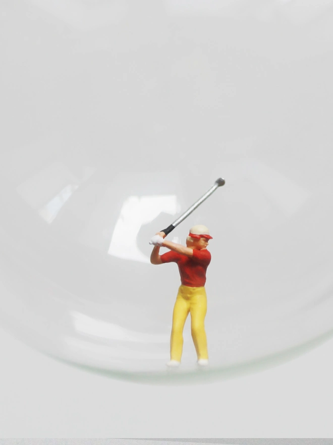 Miniature figure of a female golfer in a glass Christmas bauble - close up 
