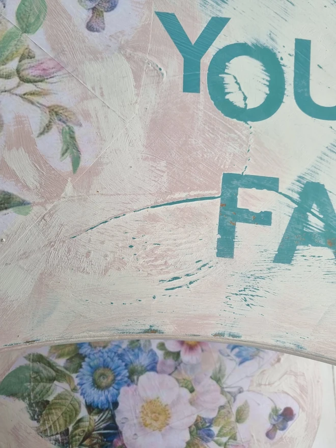 A painted dressing table in white and pale pink with large florals in blues and mauves and text in turquoise that reads 'turn your face to the sun'. The whole piece is distressed in the shabby chic style.
