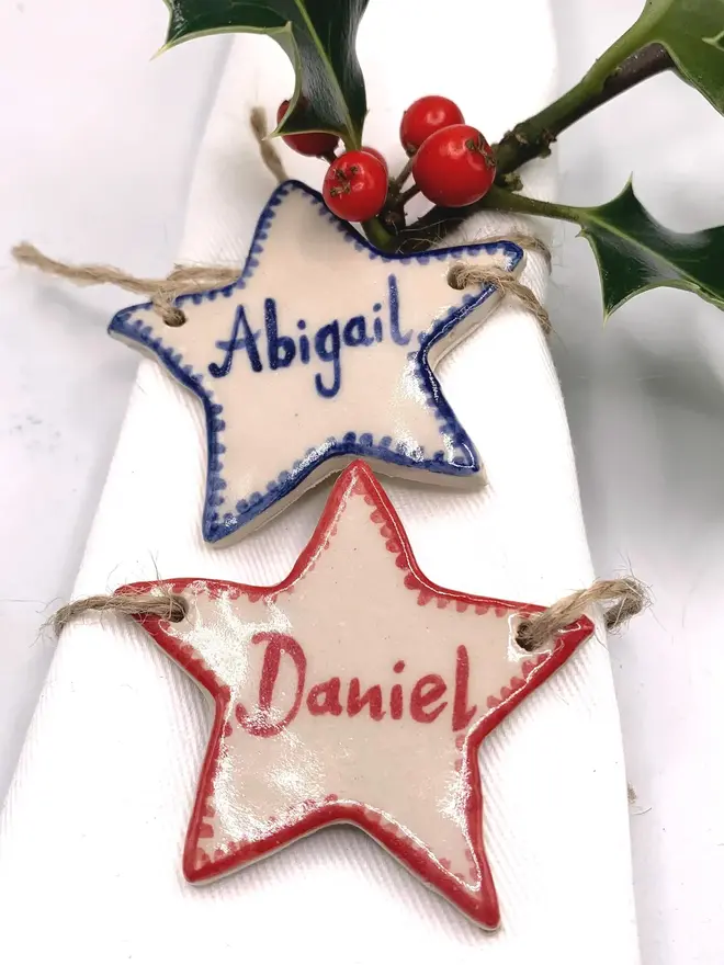 Personalised Ceramic Christmas Star Name Place Markers, a colourful ceramic start sitting on a white surface attached to a holly bush. 