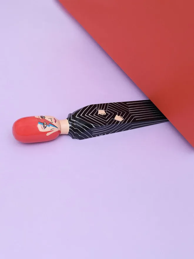 Wooden Door Stopper (Major Dave Black Outfit), a colourful wooden door stop sitting under a door.